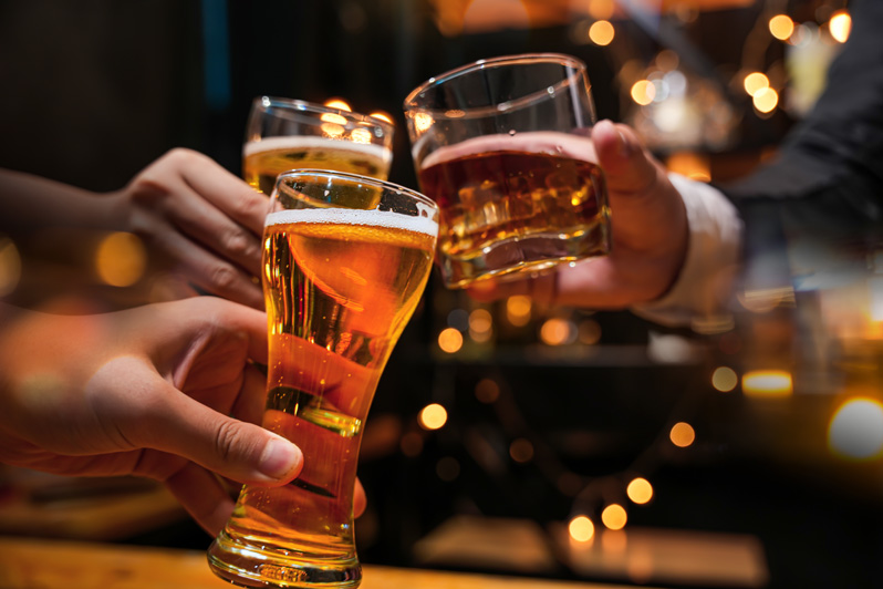 friends are happy drinking beer and clinking glasses at a bar